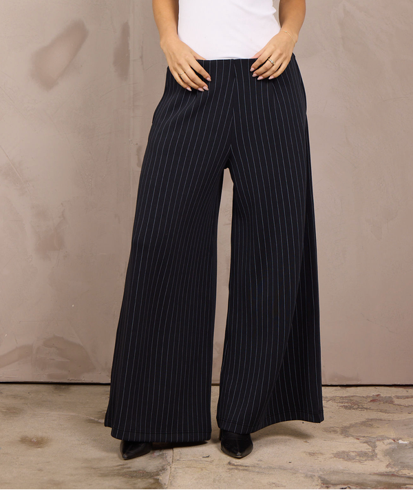 Woman wearing wide-leg pleated-front pinstripe trousers with an elastic waistband.