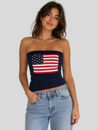 Navy knit strapless sweater tube top with American flag graphic paired with light wash denim jeans.