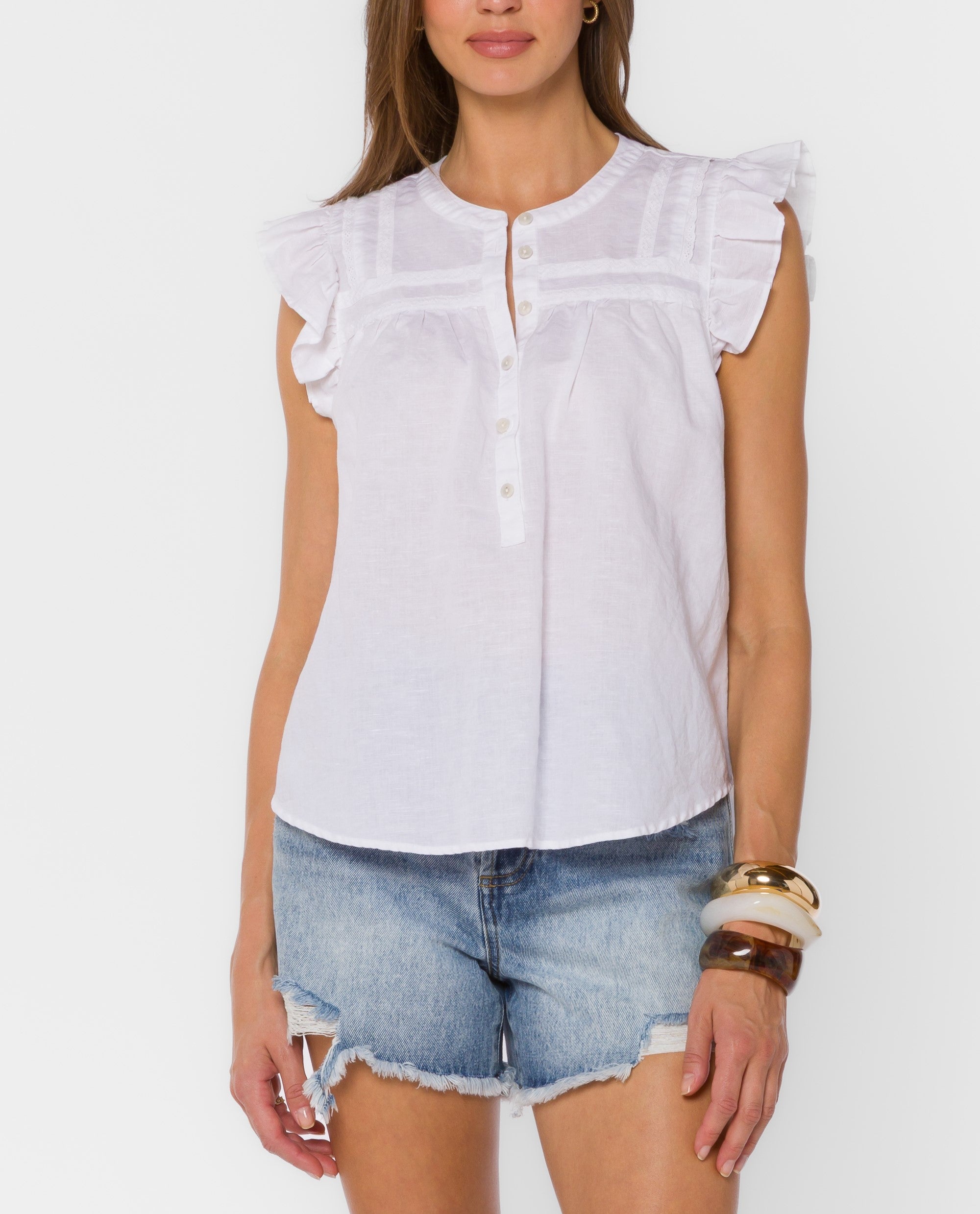 White sleeveless blouse with ruffle sleeves, button-front neckline, and delicate trim details paired with distressed denim shorts.