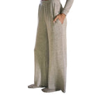 A person wearing light heather gray wide-leg knit pants with an elastic waistband and side pockets, standing indoors near a kitchen counter and rug.