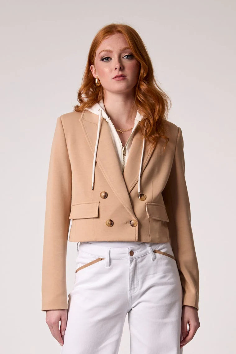 Cropped tailored blazer layered over a zip-front hoodie with structured fit, notched lapel, and double-breasted button detail, styled with high-rise pants