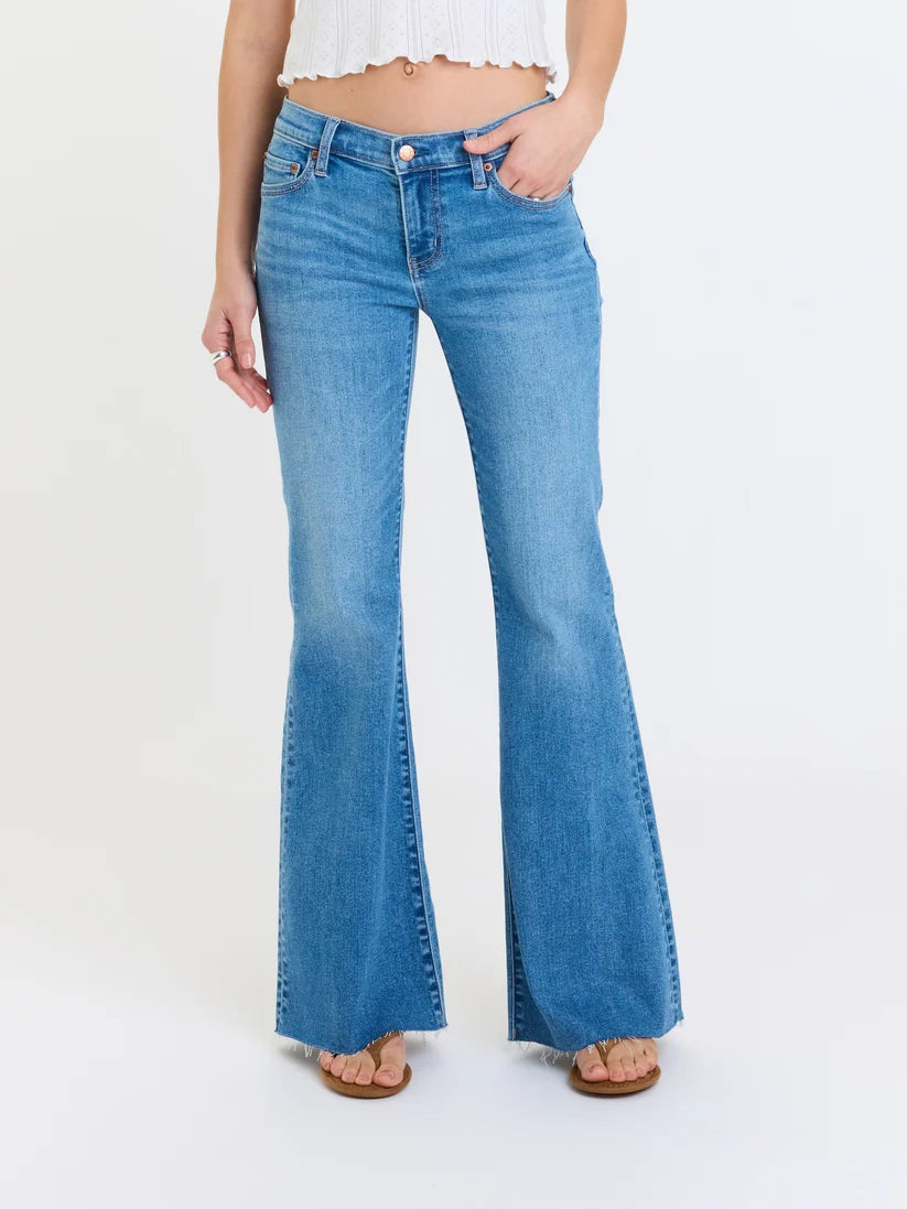 Model wearing mid-rise flare jeans with a fitted silhouette, raw hem, and medium wash denim.