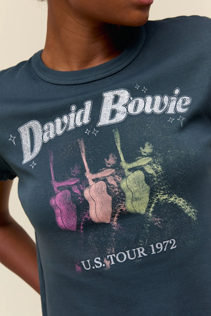 Day Dreamer Bowie Shrunken Tee Vintage Black. This cool shrunken tee features a graphic of Bowie with his guitar and his tour locations marked on the back. Accented in silver glitter.