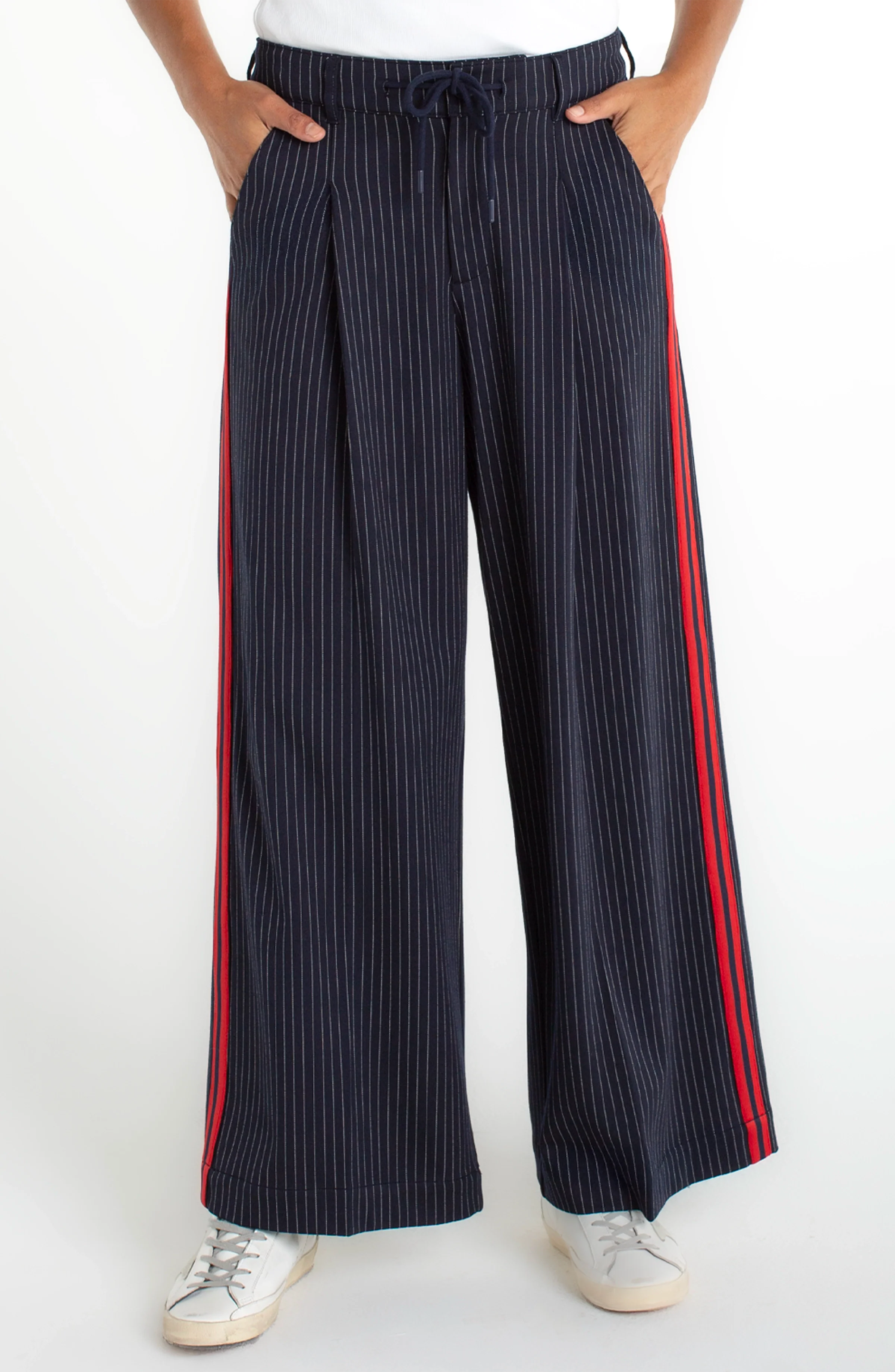 Wide leg navy pants with drawstring waist, pinstripe pattern, and red contrast side stripe styled with sneakers