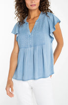 woman wearing a blue denim flutter sleeve v neck pintuck blouse
