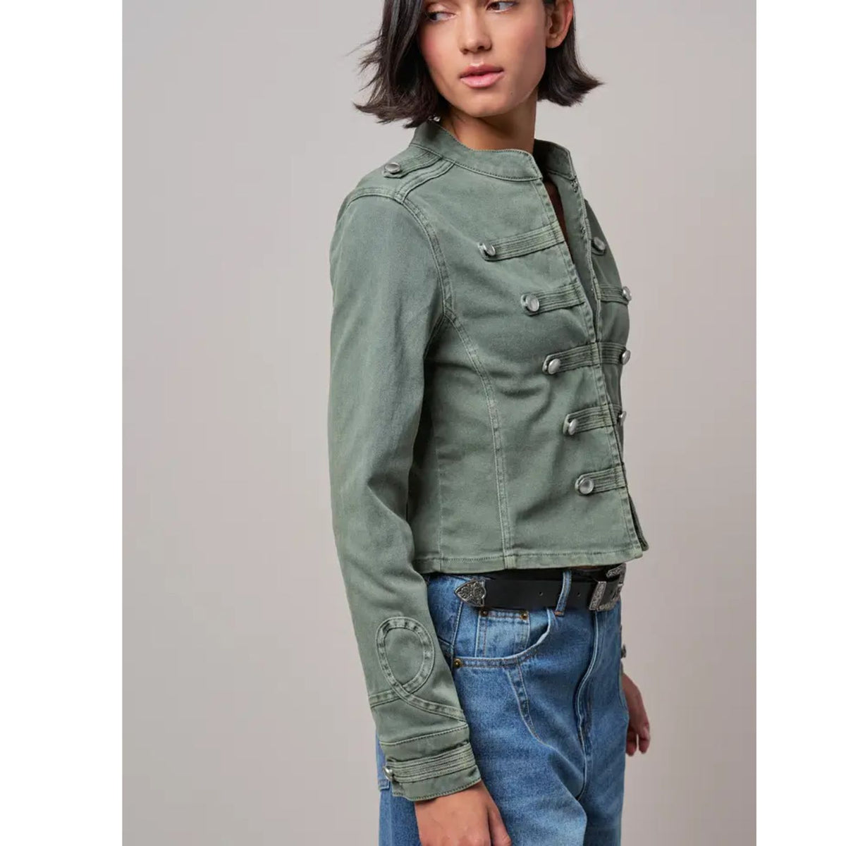 Military-inspired fitted denim jacket with a stand collar, decorative button tabs, and elbow patches