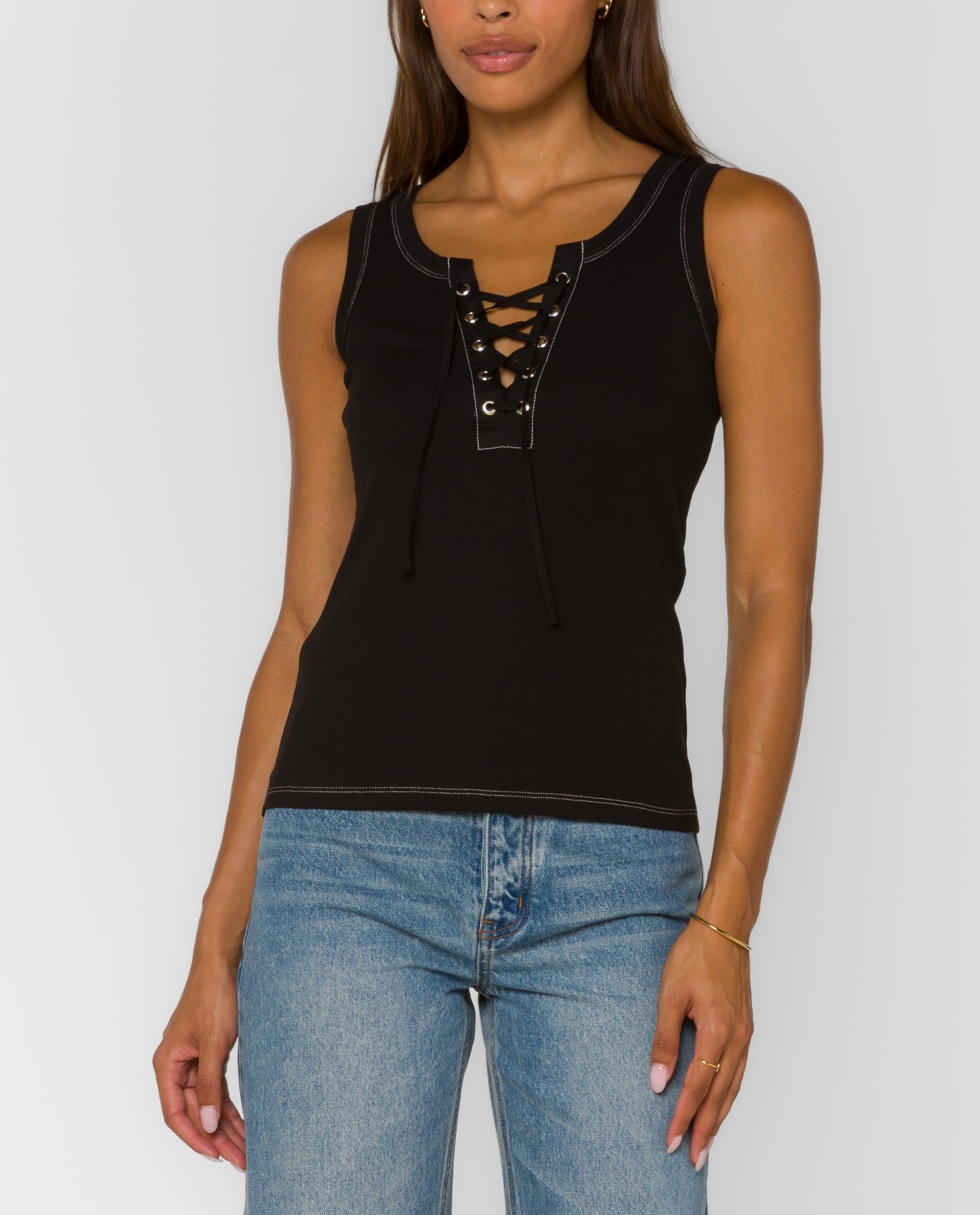 Black sleeveless lace-up tank top with contrast stitching and fitted silhouette paired with light wash jeans.