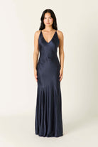 Model wearing a satin maxi slip dress with a V-neckline, thin adjustable straps, low V-back, and flowing flared hem.