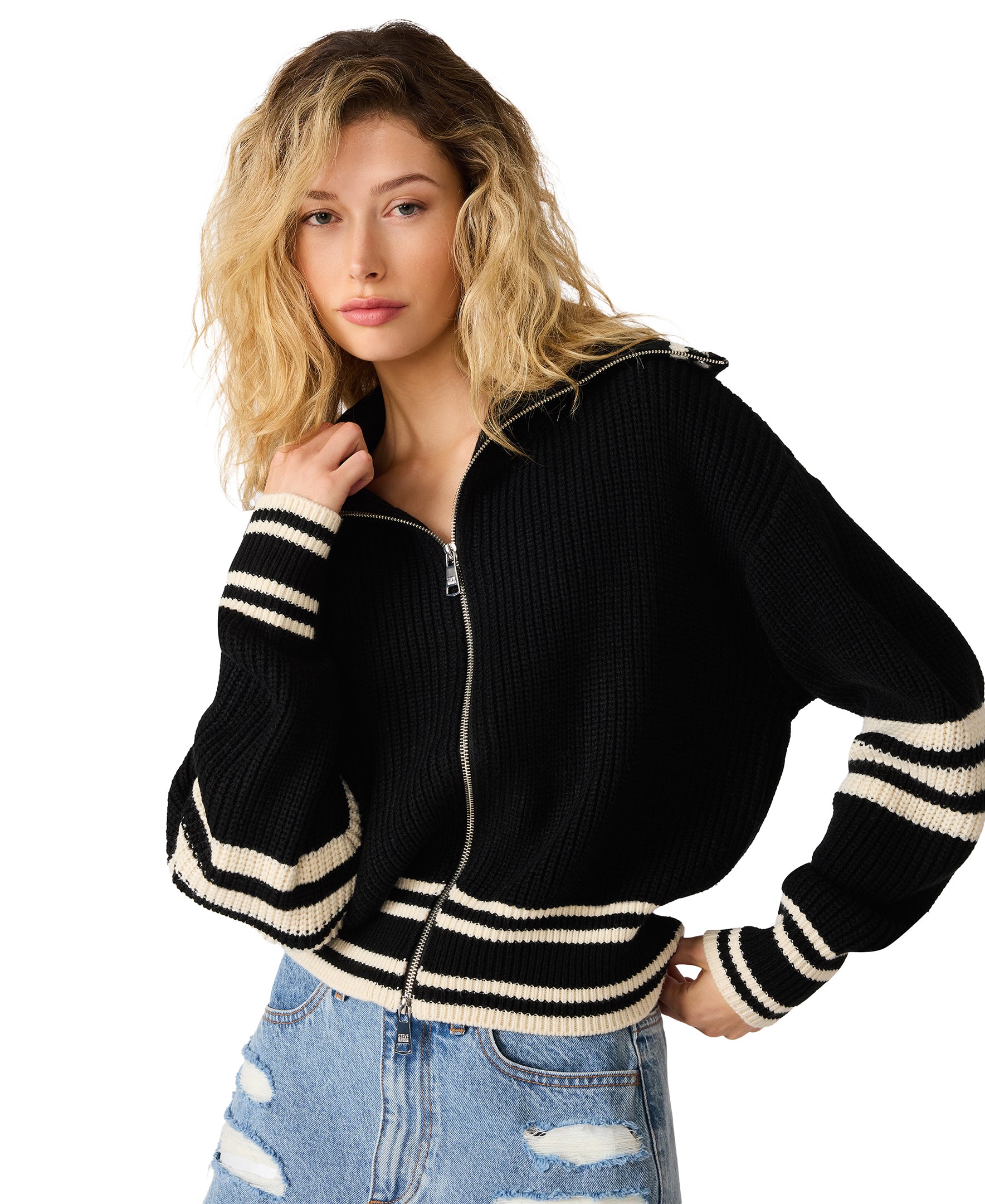 Model wearing a black ribbed zip-front sweater with contrast striped trim and a relaxed fit paired with distressed denim jeans.