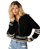 Model wearing a black ribbed zip-front sweater with contrast striped trim and a relaxed fit paired with distressed denim jeans.