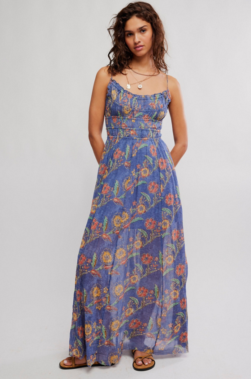 Woman wearing a smocked floral maxi dress with thin straps and a flowy full-length silhouette, styled with flat sandals
