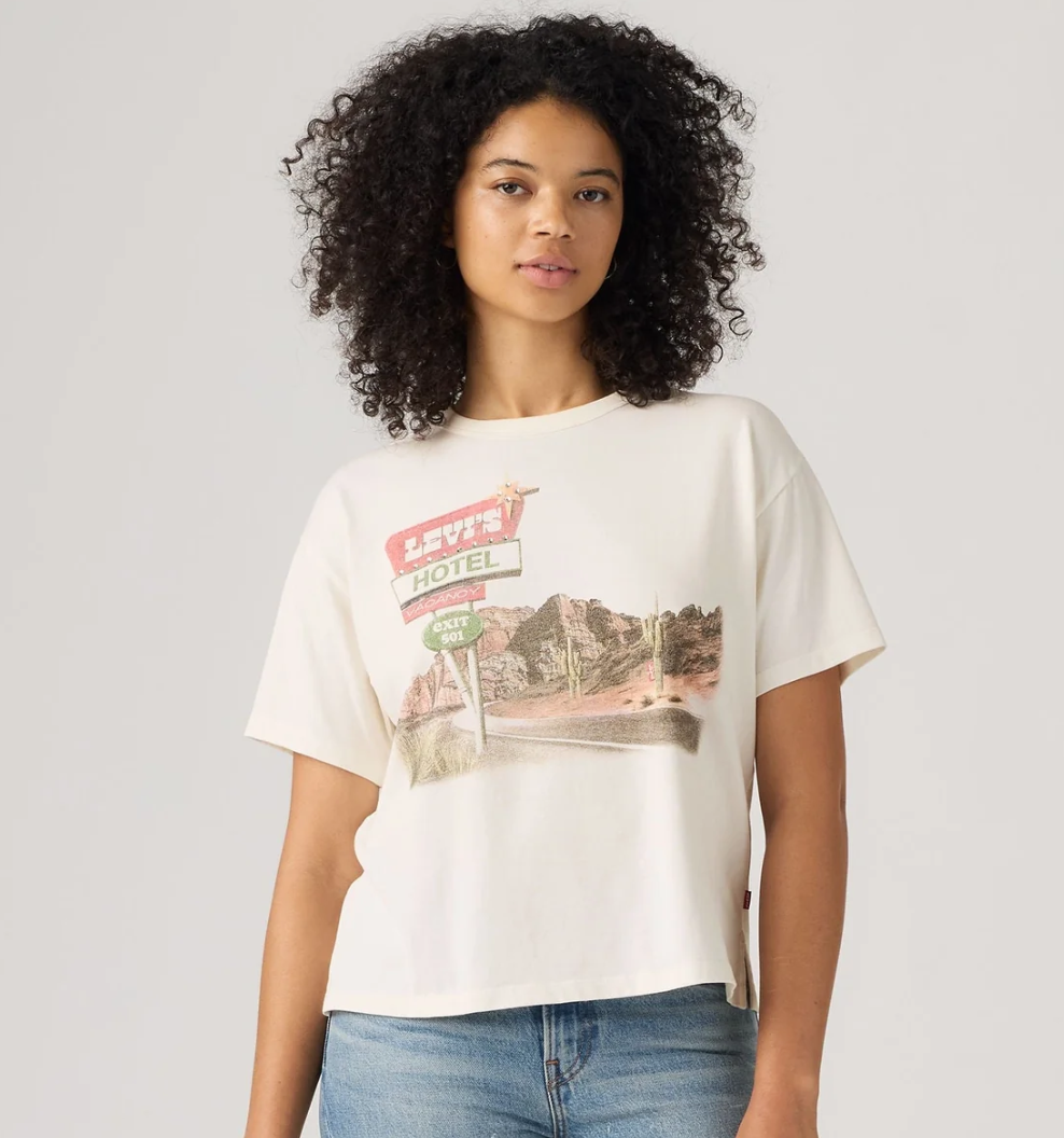 Model wearing a cream Levi's graphic short sleeve T-shirt featuring a vintage desert motel print with blue denim jeans.