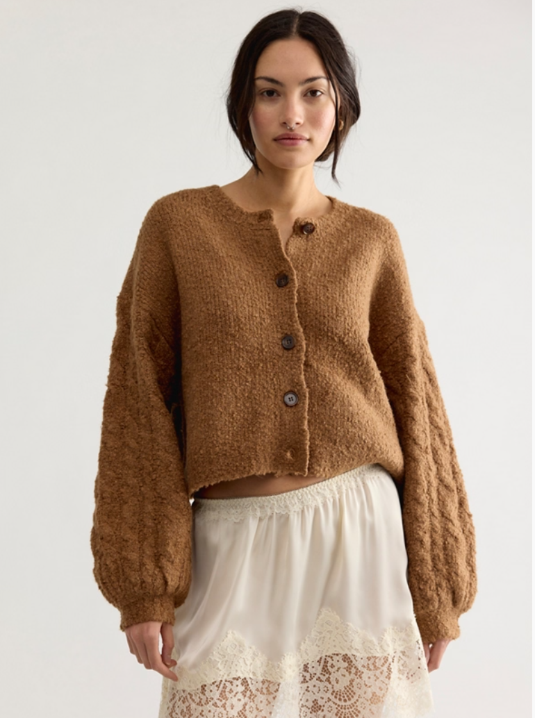 Model wearing a cropped textured knit cardigan with button-front closure, cable-knit balloon sleeves, and a relaxed fit styled over a lace-trim midi skirt.