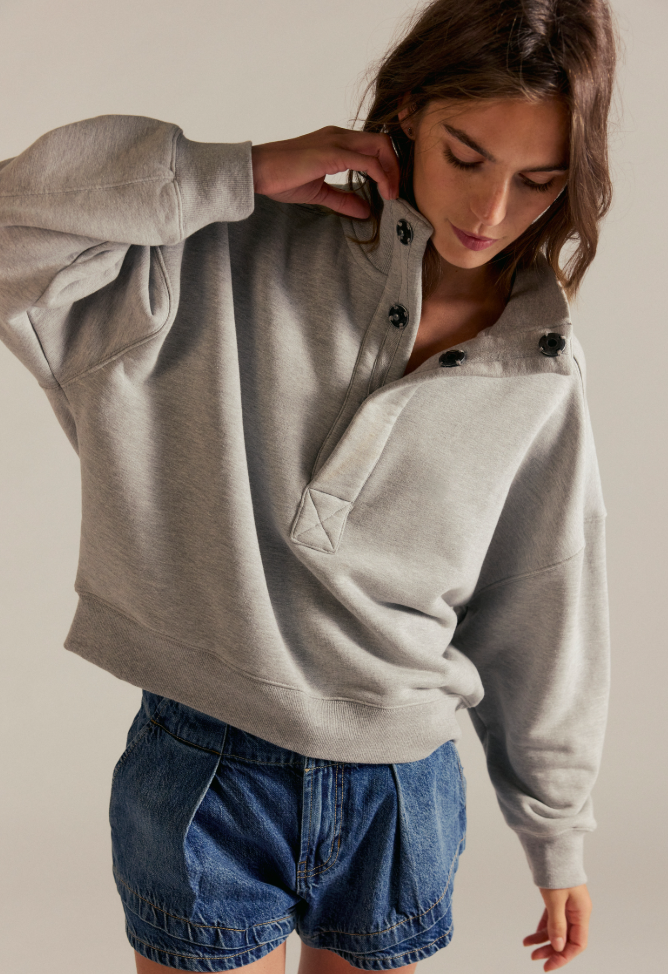 Model wearing an oversized fleece snap-neck pullover sweatshirt with a relaxed fit and long sleeves paired with denim shorts.