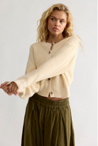 Model wearing a cropped button-front knit cardigan with a relaxed fit, ribbed trim, and long sleeves paired with a flowy skirt.