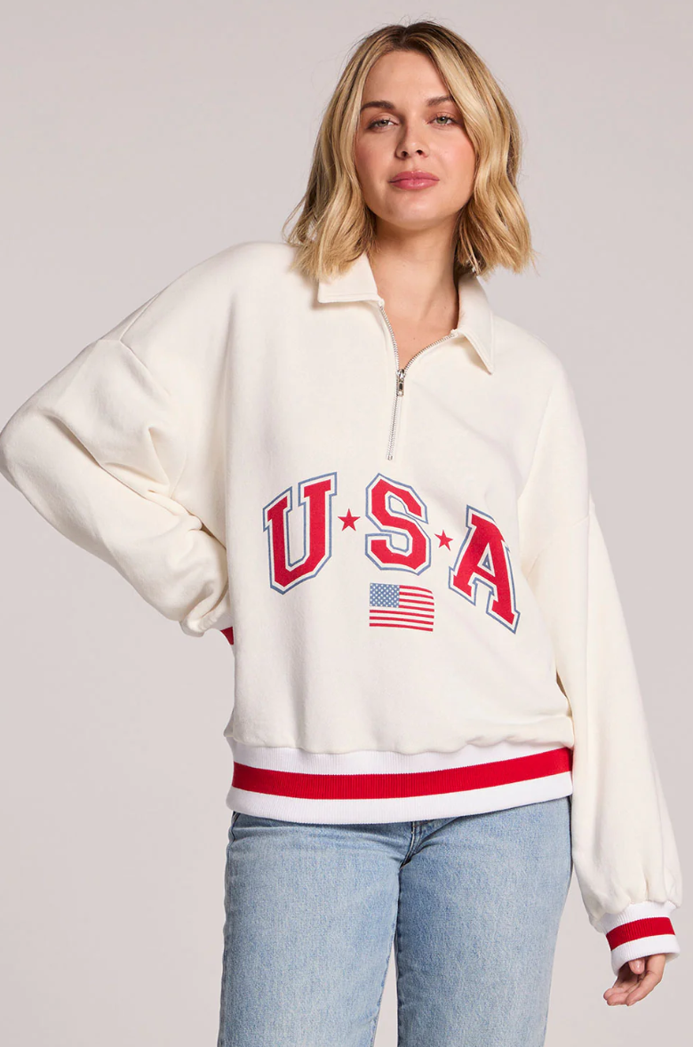 Cream quarter zip sweatshirt with USA graphic, striped ribbed trim, and relaxed fit paired with light wash denim.