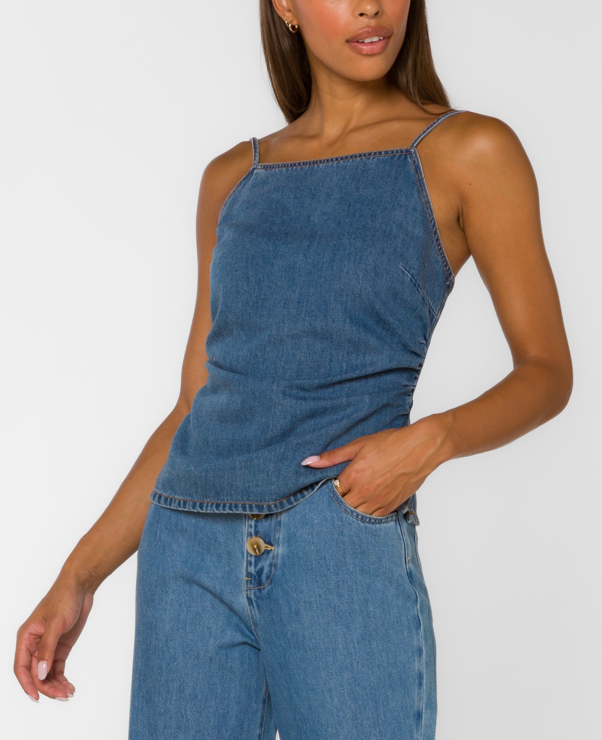 Denim camisole top with square neckline, adjustable straps, smocked back, and peplum hem paired with wide leg denim pants.