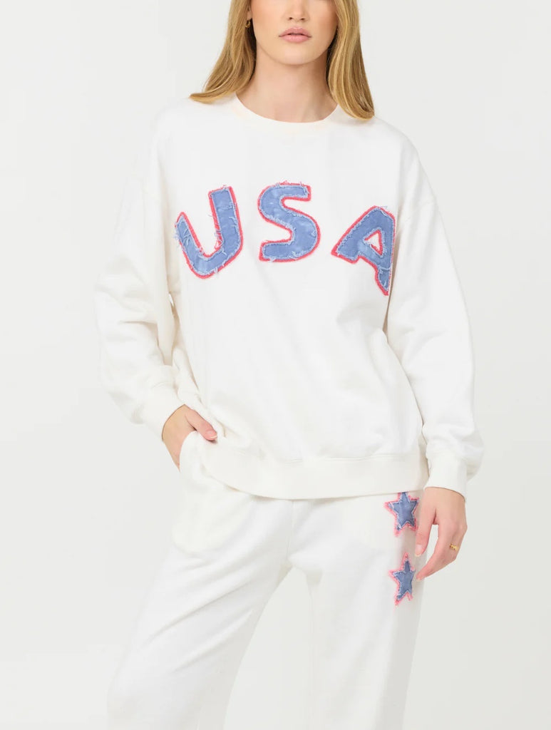 Vintage Havana USA Terry Crewneck White Blue. This cozy French terry crewneck pullover sweatshirt features a 'USA' graphic, that goes perfectly with the Star Terry Joggers for a cute sweat set.