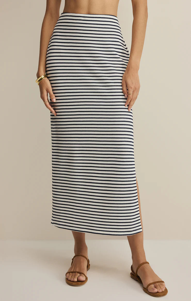 Woman wearing a striped knit midi skirt with a fitted silhouette and side slit detail, styled with flat sandals