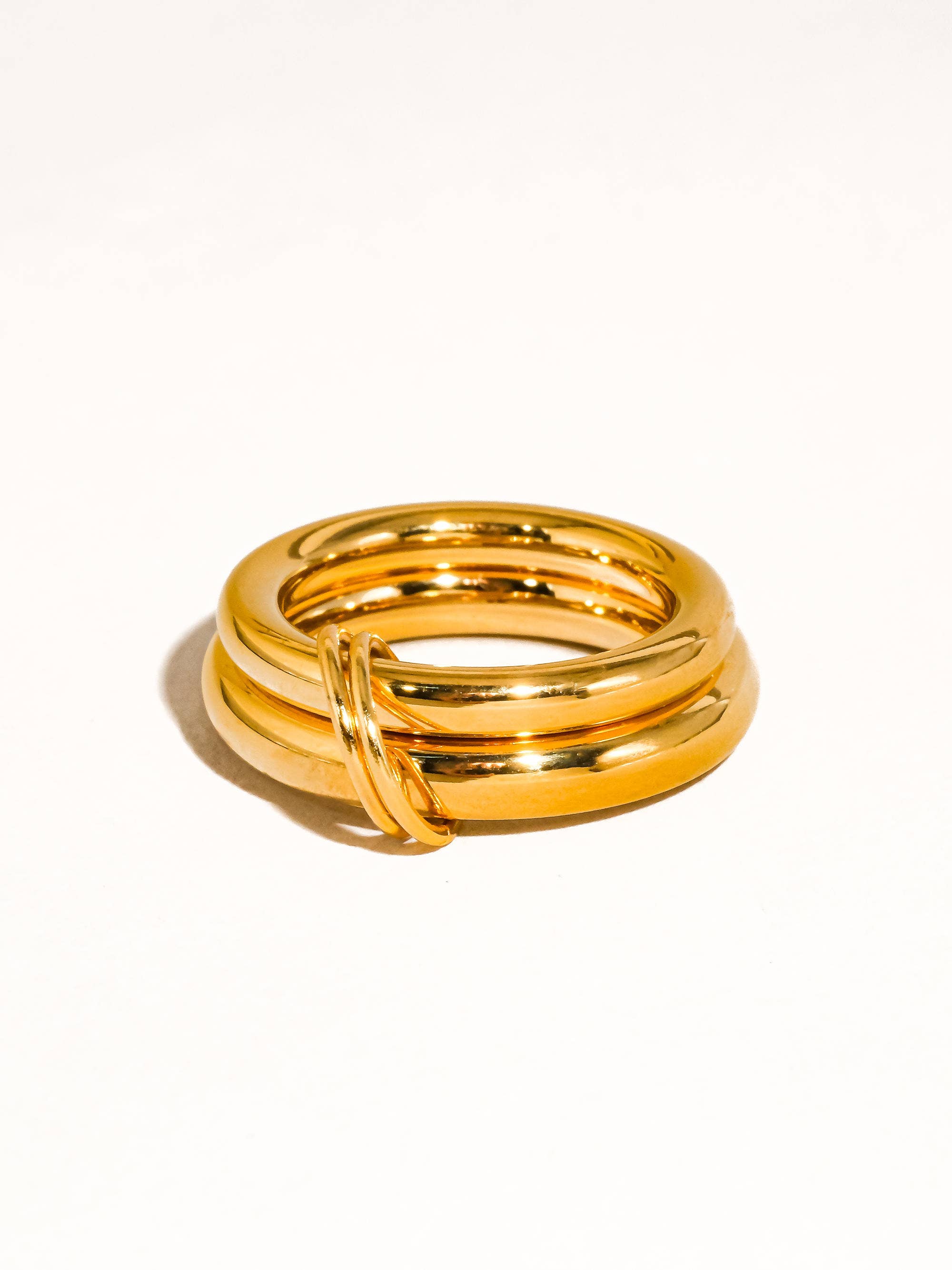 Chunky gold double-band statement ring with interlocking detail on a neutral background.