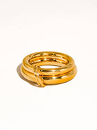 Chunky gold double-band statement ring with interlocking detail on a neutral background.