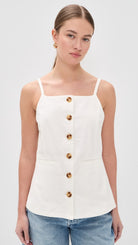 Woman wearing a sleeveless button front cami top with thin straps and a square neckline paired with denim jeans