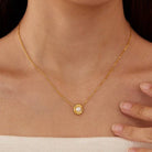 Delicate gold-tone chain necklace featuring a round pearl-inspired pendant in a bezel setting, worn on a model with a strapless knit top.