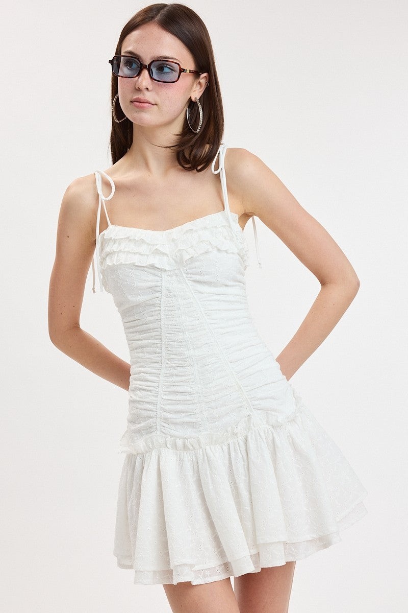 Mini dress with ruched bodice, ruffle details, tie straps, and flouncy skirt styled with sunglasses