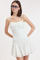 Mini dress with ruched bodice, ruffle details, tie straps, and flouncy skirt styled with sunglasses