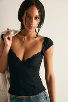 Model wearing a fitted knit top with a sweetheart neckline, lace trim, cap sleeves, and a textured finish, styled with denim.