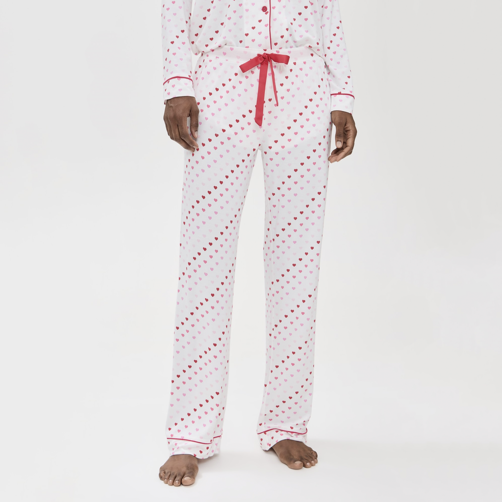 Indulge in comfort and charm with this luxe pajama set, featuring soft pink hearts and buttery fabric. The button-down top with piping details and loose-leg pants with an elastic waist offer the perfect combination of relaxation and style.