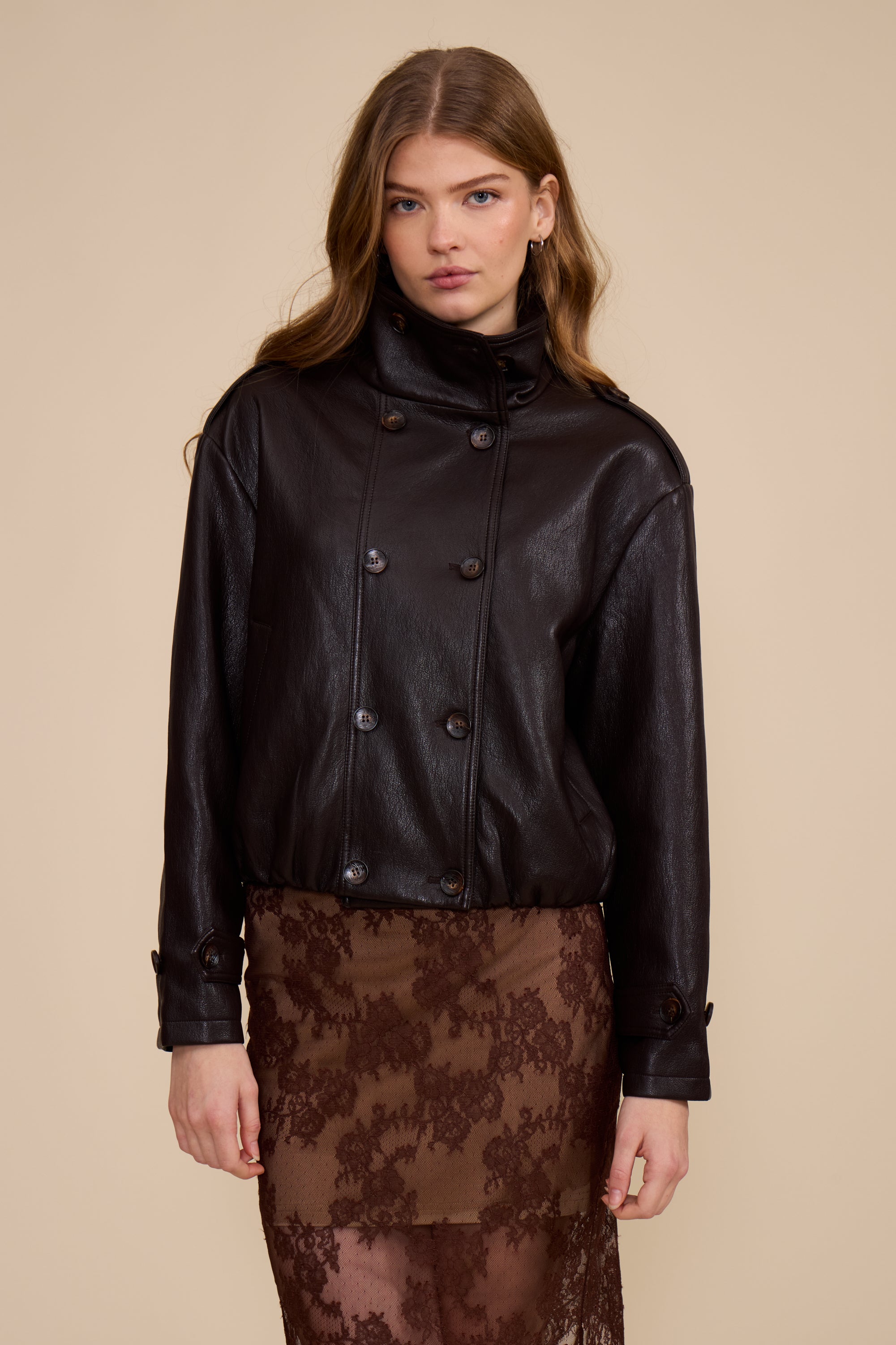Woman wearing a brown leather jacket over a brown lace dress on a beige background