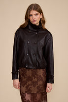 Woman wearing a brown leather jacket over a brown lace dress on a beige background