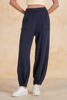 Model wearing relaxed knit jogger pants with an elastic waistband, front patch pockets, and tapered legs, styled with a ribbed tank top and sneakers.