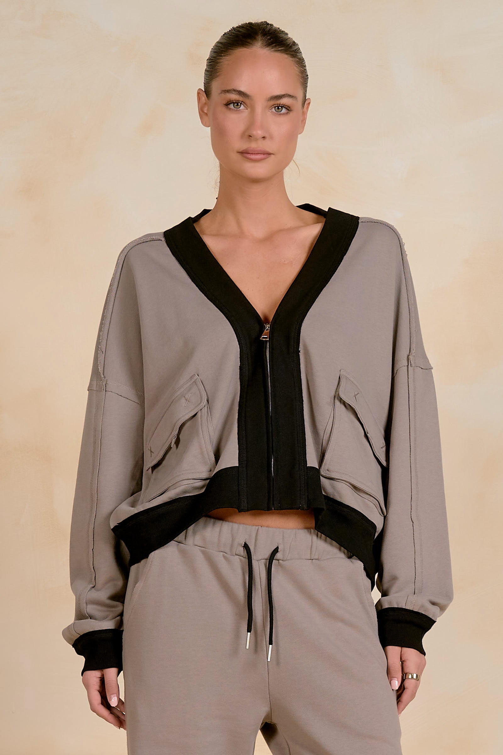 Model wearing a cropped zip-up jacket with contrast trim, utility-inspired flap pockets, and a relaxed fit, styled with matching drawstring joggers against a neutral studio background.