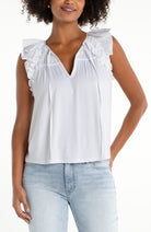 Sleeveless blouse with ruffle trim, pleated neckline, and relaxed fit styled with denim jeans