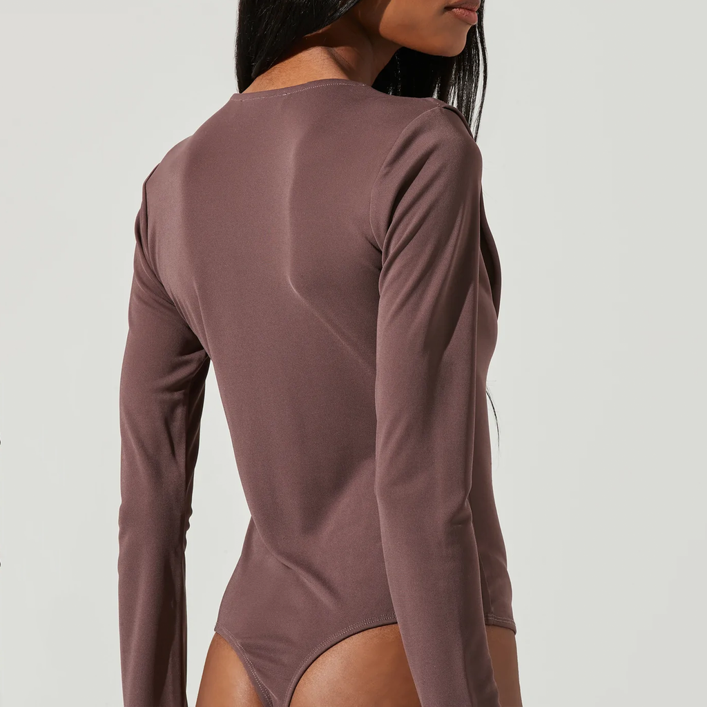 ASTR Kimberly Bodysuit. The Kimberly Bodysuit features a plunging front with a sleek, draped cowl neckline and long sleeves. Attached thong bottoms have snap button closures to stay tucked in to whatever bottoms you choose